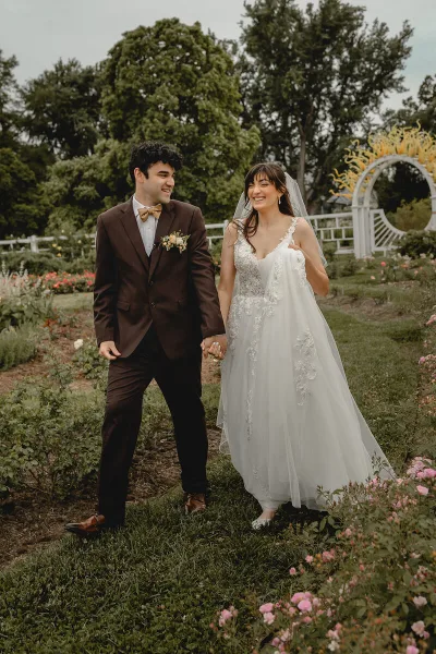 A bride and groom walking hand-in-hand through a garden with a wedding arch in the background.