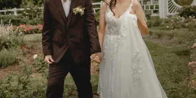 A bride and groom walking hand-in-hand through a garden with a wedding arch in the background.