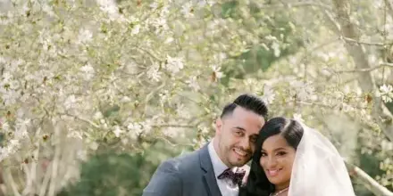 A bride and groom posing together outdoors under blooming trees, with the bride holding a floral bouquet.
