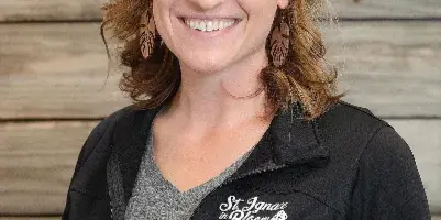 Portrait of Samantha Belonga, owner of St. Ignace in Bloom, wearing a black jacket with the business logo.