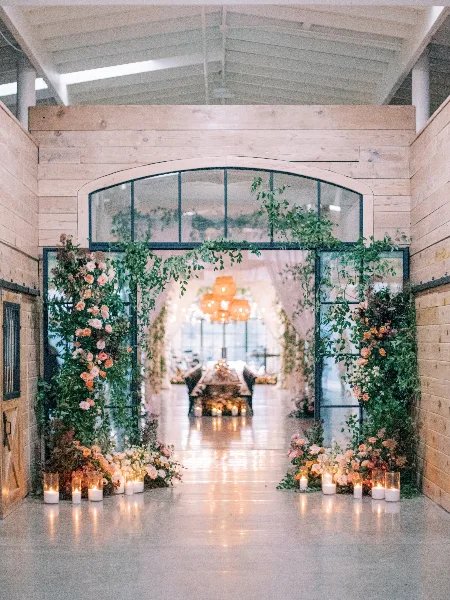 A wedding venue entrance decorated with cascading greenery and floral arrangements, with candles on the floor.