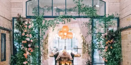 A wedding venue entrance decorated with cascading greenery and floral arrangements, with candles on the floor.