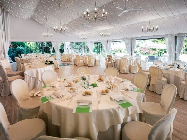 A large white marquee tent interior set up for a formal event with round tables, white tablecloths, chandeliers, and place settings.