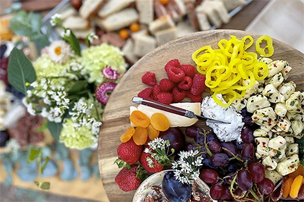 A close-up of a catering platter featuring fresh raspberries, strawberries, grapes, cheese, and crackers, garnished with small white flowers.