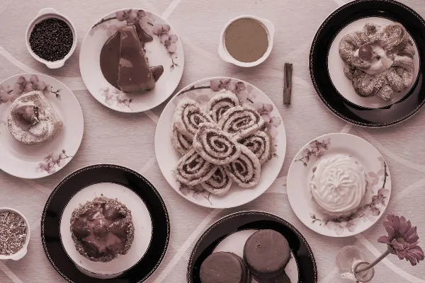 An overhead shot of an assortment of baked goods including cinnamon rolls, chocolate cake, and pastries arranged on decorative plates.