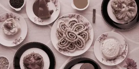 An overhead shot of an assortment of baked goods including cinnamon rolls, chocolate cake, and pastries arranged on decorative plates.