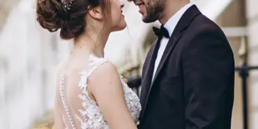 A bride and groom smiling at each other in a romantic setting with blurred lights in the background.