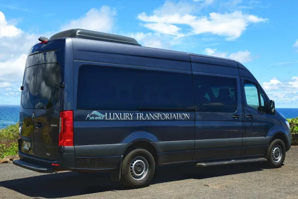 Dark blue Mercedes Sprinter van with Kauai Luxury Transportation branding parked near the ocean