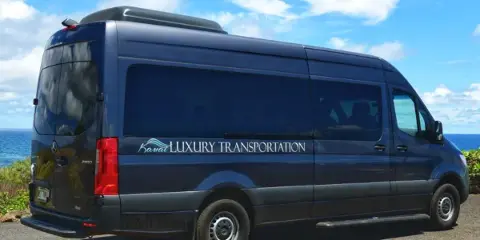 Dark blue Mercedes Sprinter van with Kauai Luxury Transportation branding parked near the ocean