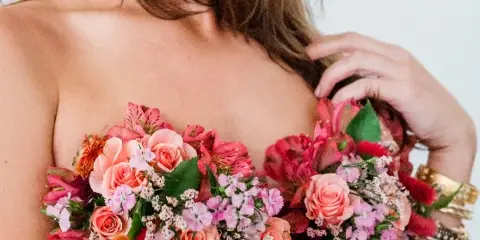 A close-up of a woman holding a large, colorful floral bouquet with pink roses and alstroemeria.