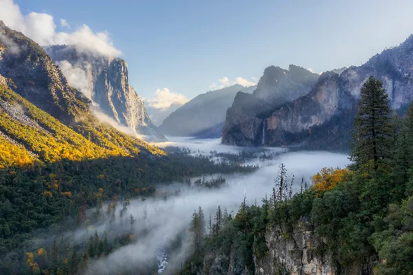 A scenic landscape photograph of a mountain valley with fog and trees.