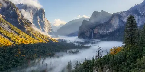 A scenic landscape photograph of a mountain valley with fog and trees.