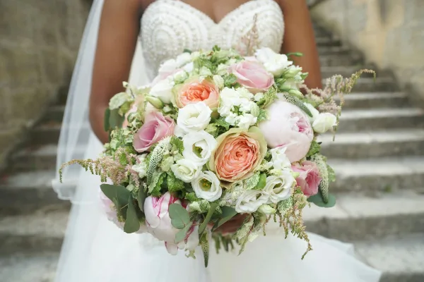 A bride in a white dress holding a large bouquet of pink and white flowers with greenery.