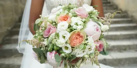 A bride in a white dress holding a large bouquet of pink and white flowers with greenery.