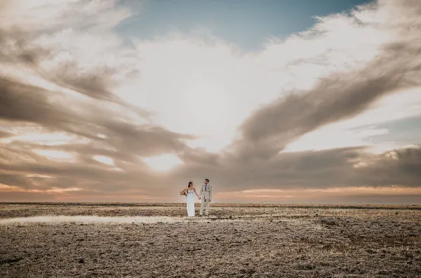 A bride and groom standing in a field under a dramatic sky