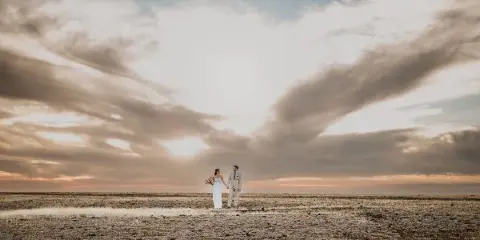 A bride and groom standing in a field under a dramatic sky