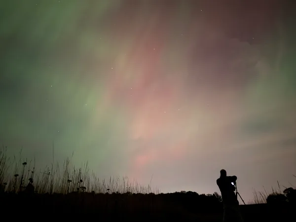 A silhouetted videographer filming the night sky with a camera on a tripod.