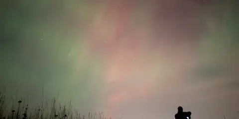 A silhouetted videographer filming the night sky with a camera on a tripod.