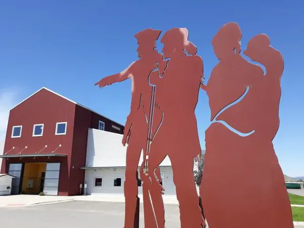 Red and white fairgrounds event building with a large red metal sculpture of figures in the foreground under a blue sky