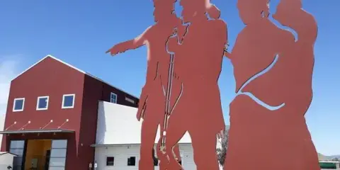 Red and white fairgrounds event building with a large red metal sculpture of figures in the foreground under a blue sky