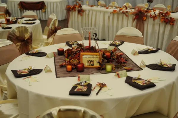 A decorated round banquet table with white linens, autumn-themed centerpieces, and place settings in a wedding reception hall.