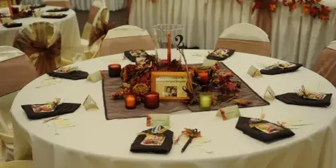 A decorated round banquet table with white linens, autumn-themed centerpieces, and place settings in a wedding reception hall.