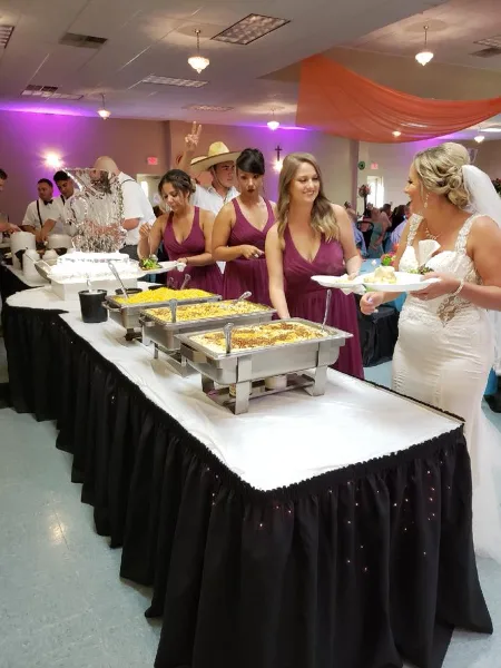 A bride and bridesmaids serving food from a buffet line at a wedding reception.