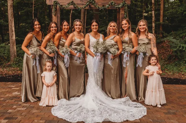 A bride and bridesmaids in champagne dresses posing in a forest setting with a wooden structure.