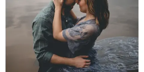 A professional engagement photograph of a couple embracing near a body of water, with the word 'PHOTOGRAPHY' displayed at the bottom.