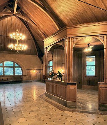 Interior of the Keokuk Union Depot waiting room featuring a high wooden cathedral ceiling, chandeliers, and an octagonal wooden ticket booth.