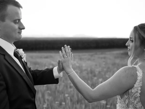 Black and white photograph of a bride and groom holding hands in a field.