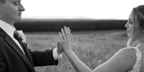Black and white photograph of a bride and groom holding hands in a field.
