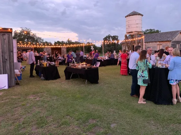 Outdoor evening event at Pioneer Village with string lights, tables, and guests near historic structures.