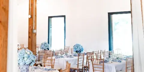 A wedding reception hall with round tables, white linens, blue floral centerpieces, and ceiling drapery.