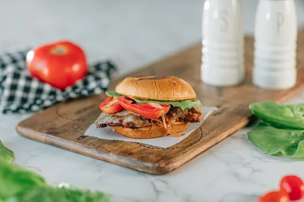 A close-up photograph of a sandwich with lettuce and tomato served on a wooden cutting board.