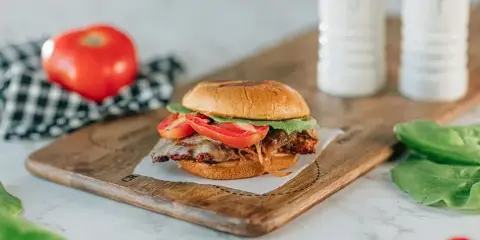 A close-up photograph of a sandwich with lettuce and tomato served on a wooden cutting board.