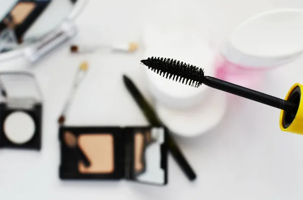 A close-up of a mascara wand and makeup palette on a white surface.