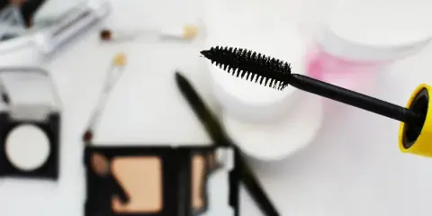 A close-up of a mascara wand and makeup palette on a white surface.