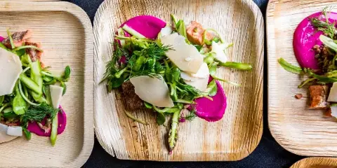 Overhead view of multiple plated appetizers with salmon, greens, and cheese on biodegradable plates.