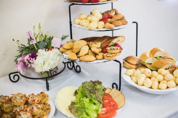 A catering table featuring a tiered stand of pastries, a plate of sandwiches, and a platter of appetizers.