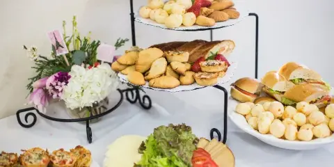 A catering table featuring a tiered stand of pastries, a plate of sandwiches, and a platter of appetizers.