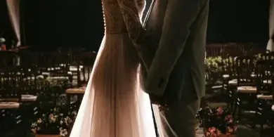 A bride and groom standing face-to-face in a large event tent with string lights and set tables.