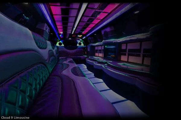 Interior view of a luxury party bus with purple ambient lighting, plush seating, and a bar area.