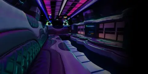 Interior view of a luxury party bus with purple ambient lighting, plush seating, and a bar area.