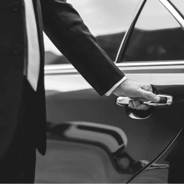 A professional chauffeur in a suit opening the door of a luxury sedan.
