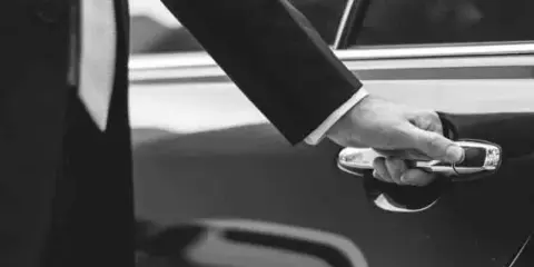 A professional chauffeur in a suit opening the door of a luxury sedan.