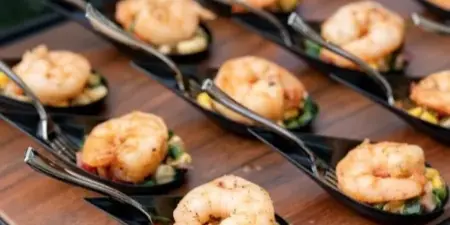 Tray of shrimp appetizers on black serving spoons arranged over a wooden board at an outdoor event.