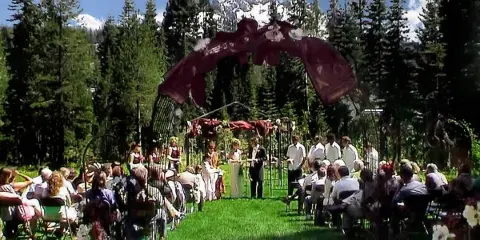 Outdoor wedding ceremony in a forest clearing with a decorated arch and mountain views.