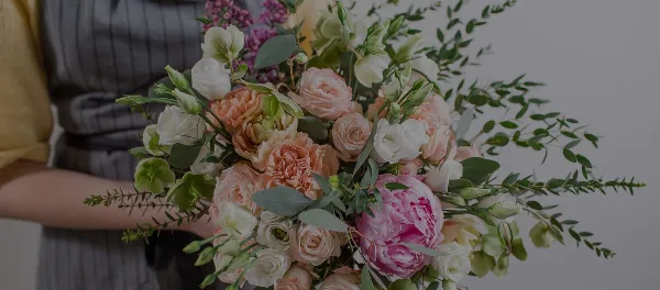 A close-up photograph of a hand-held floral bouquet containing pink and white roses, a large pink peony, and green eucalyptus stems.