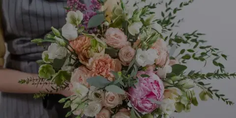 A close-up photograph of a hand-held floral bouquet containing pink and white roses, a large pink peony, and green eucalyptus stems.